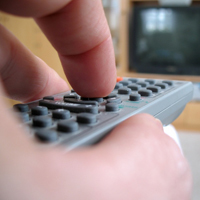 Fernbedienung in einer Hand zeigt auf einen Fernseher