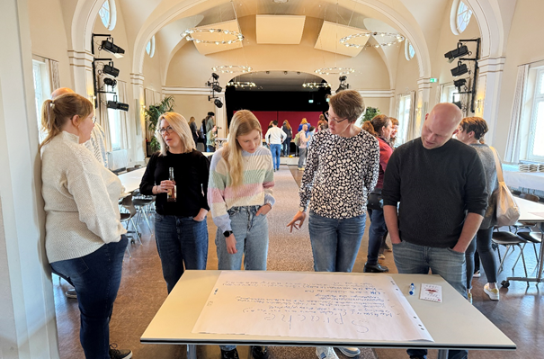 Mehrere Menschen schauen auf eine Tafel die auf dem Tisch liegt.