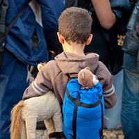 Flüchtlingskind mit Rucksack und Kuscheltier