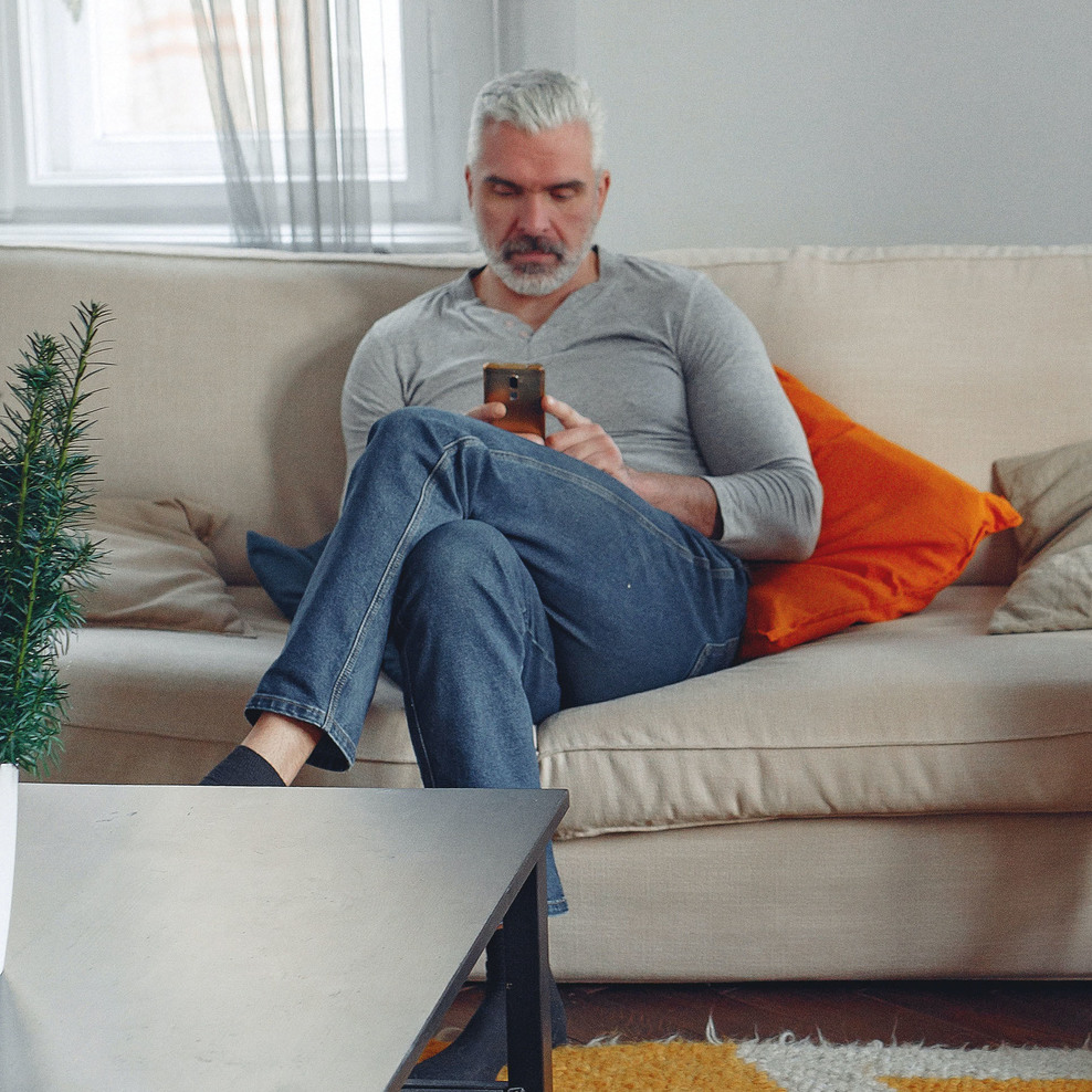 Ein Mann sitzt mit einem Smartphone in der Hand auf einem Sofa.