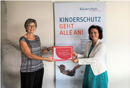 Dr. Carola Reimann und Andrea Buskotte stehen vor dem Plakat "Kinderschutz geht alle an!"