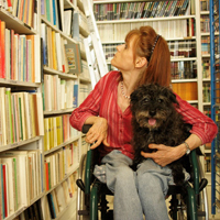 Frau im Rollstuhl sucht in einer Bibliothek nach einem Buch