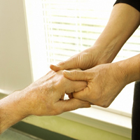 Betreuerin hält Hand einer älteren Person